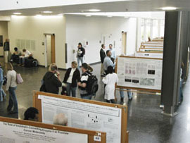 Many people standing in the medical education research facility looking at posters and tlaking