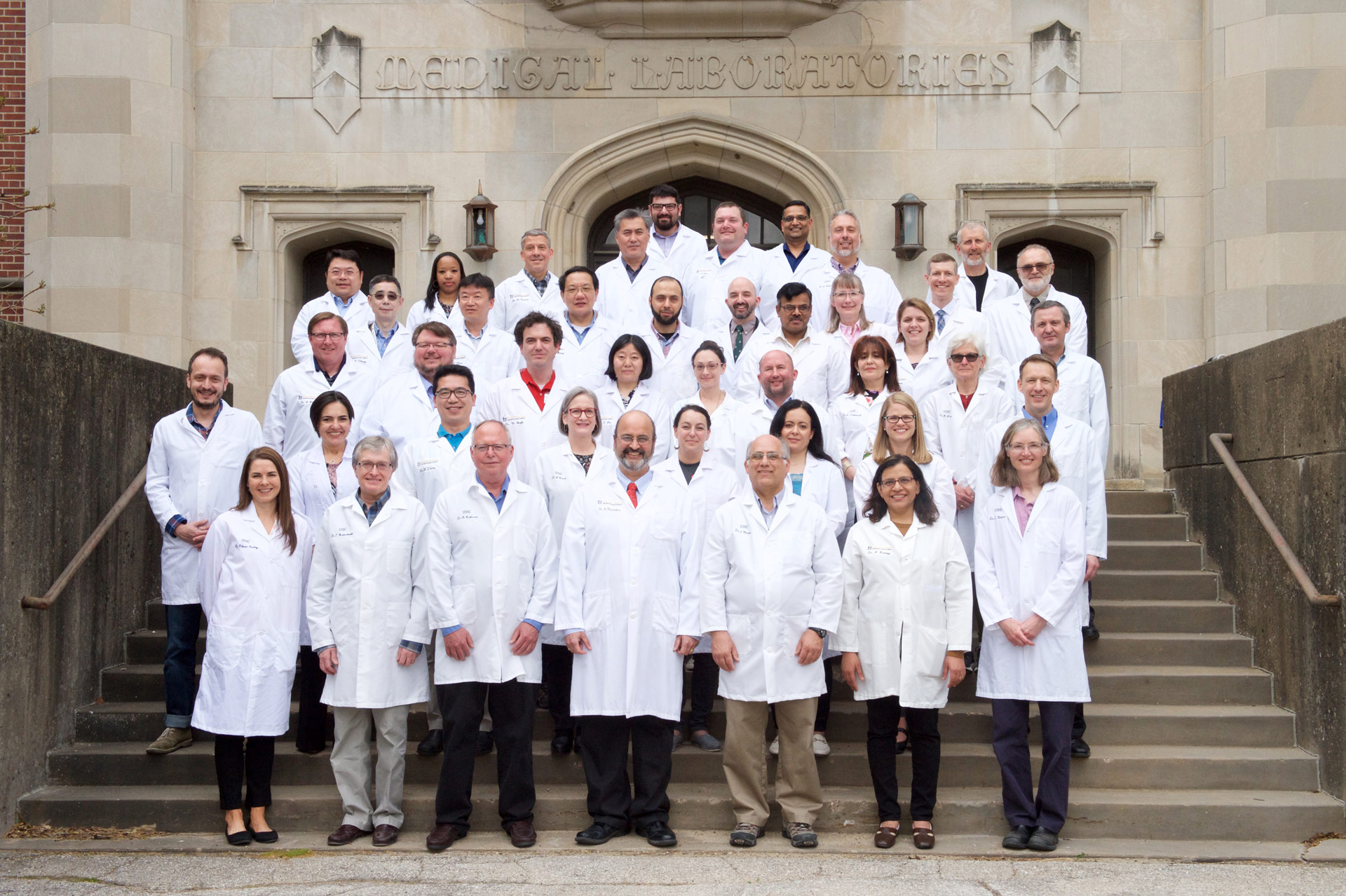 Pathology faculty in lab coats standing on the stairs outside of the medical research labs