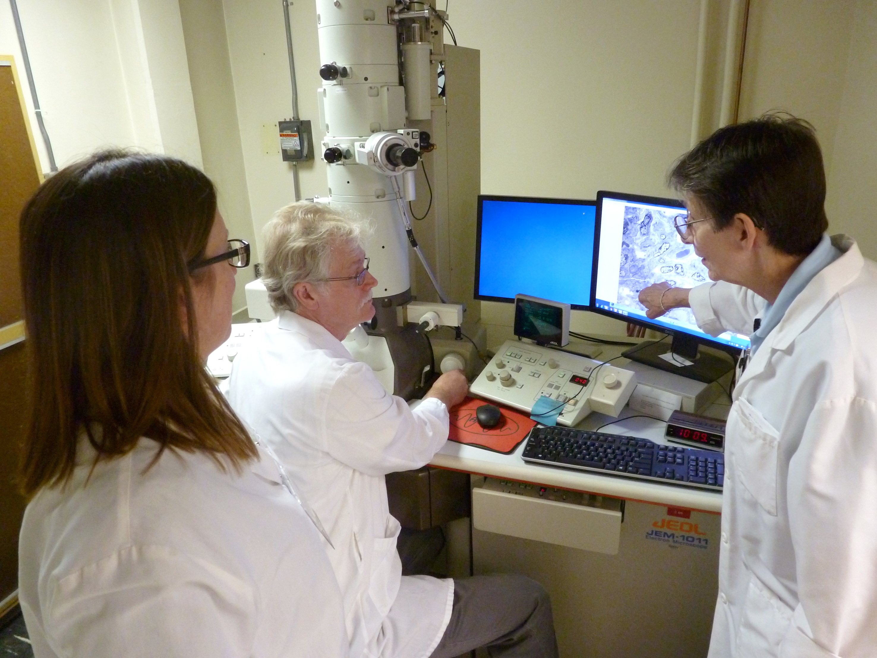 Three people looking at an electron microscope