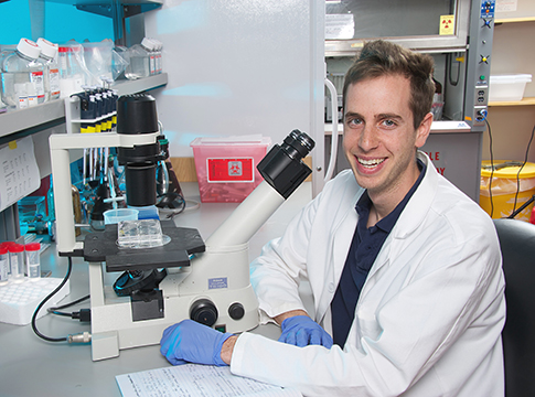 A fellow smiling, sitting near a microscope