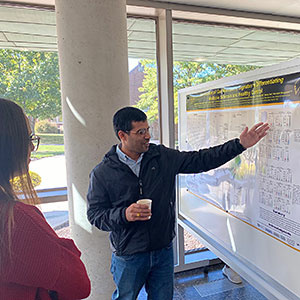 A person gesturing at a research poster, explaining it
