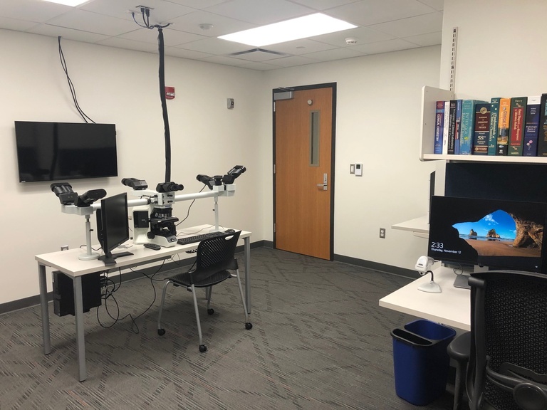 A room with microscopes, computers, books, and presentation screen