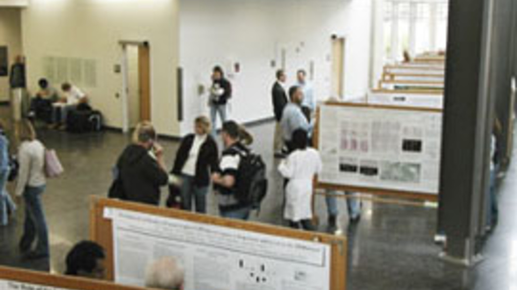 Many people standing in the medical education research facility looking at posters and tlaking